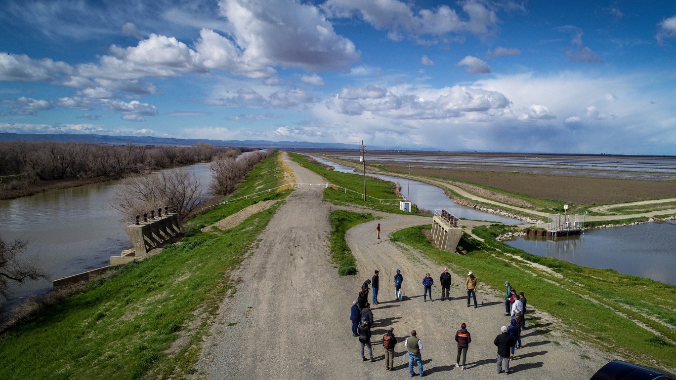 A circle of people gather near a floodplain.